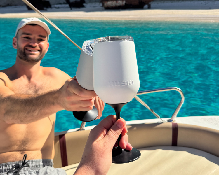 Man on a boat holding a white Huski Wine Tumbler 2.0 with TwistLock stem attached, blue water in background